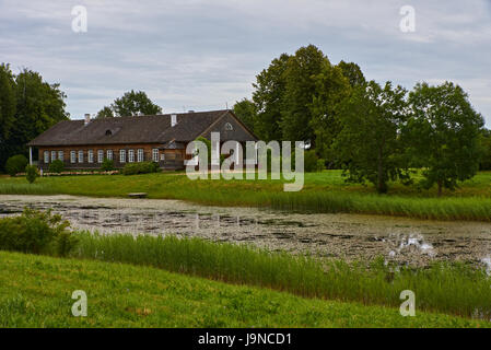 Marchande en bois maison entourée d'arbres. Les arbres sont élevés. Dans l'avant-plan pré et sentier pédestre. La Russie, région de Pskov, l'été Banque D'Images