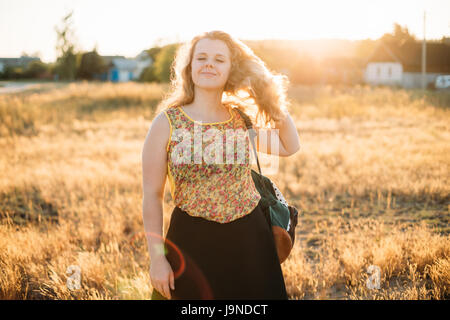 Portrait of Young Pretty Woman Taille Plus Heureux fille femme aux yeux clos, de longs cheveux bruns ondulés et son sac à dos en été Meadow Banque D'Images