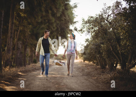 Toute la longueur de cheerful couple carrying basket en marchant sur un chemin de terre à l'Olive Farm Banque D'Images