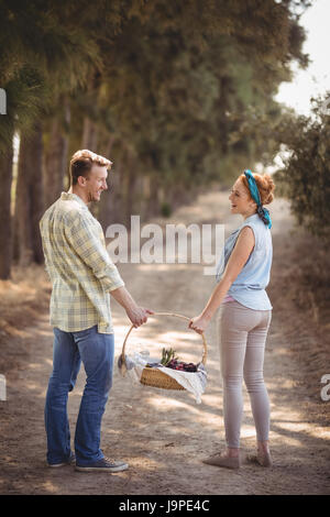 Vue arrière du cheerful young couple carrying basket sur chemin de terre au niveau de l'exploitation Banque D'Images