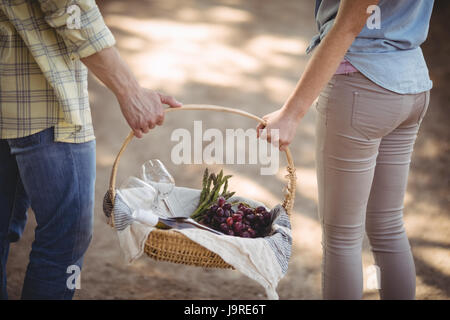 Mid section of couple carrying basket sur chemin de terre au niveau de l'exploitation Banque D'Images