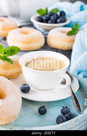Tasse de café et de beignets faits maison avec du sucre en poudre et de bleuets frais sur fond gris clair. Focus sélectif. Banque D'Images
