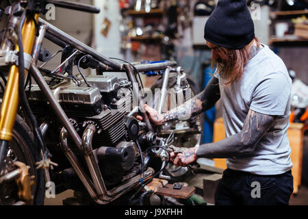 Portrait de l'accent tattooed man travaillant dans un garage moto personnalisation et la réparation de pièces cassées Banque D'Images