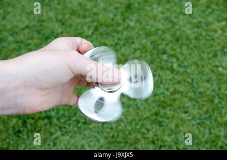 Une childs hand holding a silver spinning fidget spinner sur fond vert Banque D'Images