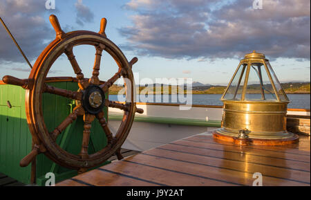 La roue du navire et de la boussole habitacle à bord d'un vieux gréement, prises tard dans la soirée dans une douce lumière dorée, à la recherche sur Kerrera en Ecosse Banque D'Images