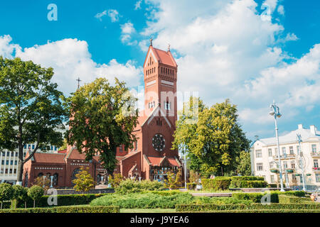 Minsk, Belarus. Vue de la façade principale de l'Église catholique romaine des Saints Simon et Helena ou Eglise rouge entre les arbres verts en été Journée ensoleillée sous Blue Banque D'Images