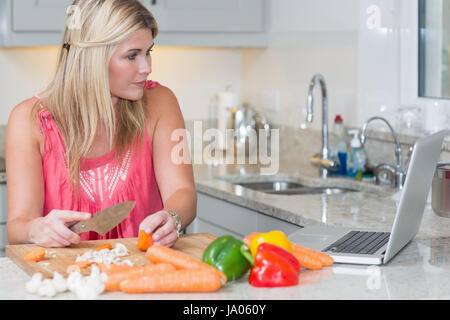 La cuisine femme en regardant ordinateur portable dans la cuisine à la maison Banque D'Images