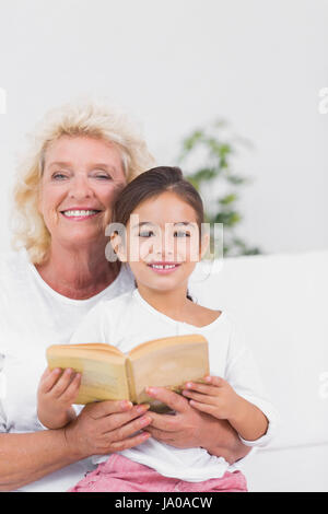 Petite fille souriante et grand-mère la lecture d'un roman ensemble sur le canapé Banque D'Images