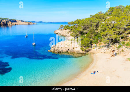 Couple de personnes non identifiée de bronzer sur une belle plage de Cala Salada, célèbre pour ses eaux cristallines de la mer d'azur, l'eau de l'île d'Ibiza, Espagne Banque D'Images