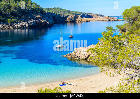 Couple de personnes non identifiée de bronzer sur une belle plage de Cala Salada, célèbre pour ses eaux cristallines de la mer d'azur, l'eau de l'île d'Ibiza, Espagne Banque D'Images