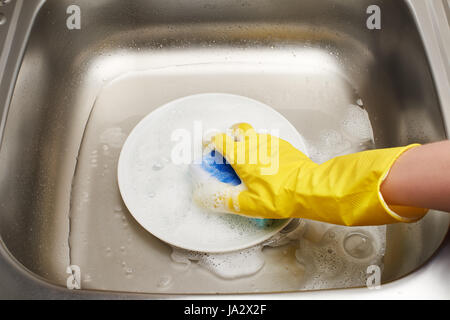 Image main de femme libre de gant en caoutchouc de protection jaune en lave plaque blanche avec une éponge de nettoyage bleu contre l'évier de cuisine Banque D'Images