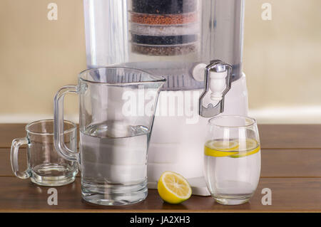 Système de filtre de purificateur d'eau avec deux verres d'eau un rempli jusqu'à ce milieu avec un citron à l'intérieur et d'un pichet vide sur la table en bois Banque D'Images