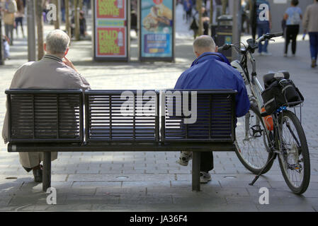 Assis sur un banc, vu de derrière deux hommes d'âge moyen et un vélo Banque D'Images