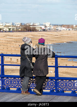 Deux visiteurs en manteaux et chapeaux admirant vue depuis la jetée d''Eastbourne sur Cold spring day, Eastbourne, East Sussex, Angleterre, Royaume-Uni. Banque D'Images