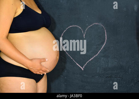 Une femme enceinte debout près d'un coeur dessiné sur un tableau. Banque D'Images