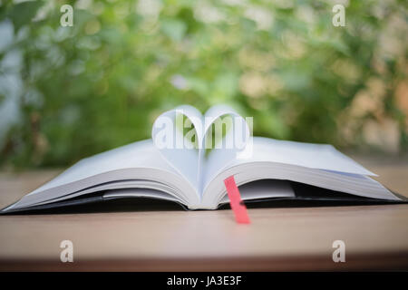 Livre ouvert sur la table en bois sur fond naturel. Coeur book page , flou et soft focus Banque D'Images