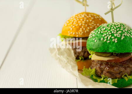 Hamburgers de petits pains vert et jaune sur le tableau en bois blanc, selective focus Banque D'Images