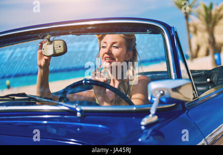 Beautiful woman applying lipstick in a retro cabriolet voiture près de la mer Banque D'Images