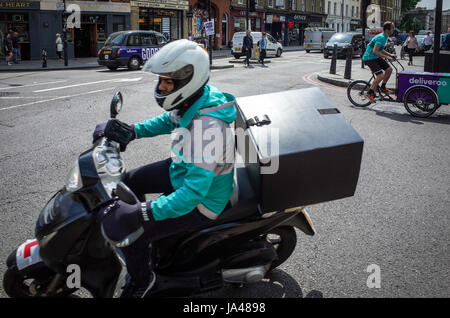 Deux Deliveroo livraison alimentaire couriers passer dans le centre de Londres, l'une sur un scooter, l'autre sur un vélo cargo Banque D'Images