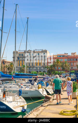 Vue arrière d'un couple d'âge moyen en vacances en longeant un quai sur le bord de la Méditerranée à Cagliari, Sardaigne. Banque D'Images