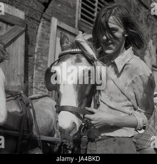 1971, historique, un jeune homme à poil long totter ou un homme à poil long tient la tête de son cheval devant les arches de chemin de fer, South London, Englod, Royaume-Uni. Banque D'Images