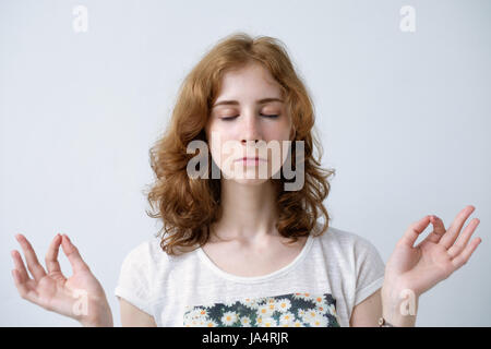 Girl with red hair holding doigts ensemble. Les yeux fermés. Méditer ou faire un voeu, essayant de se calmer. Banque D'Images