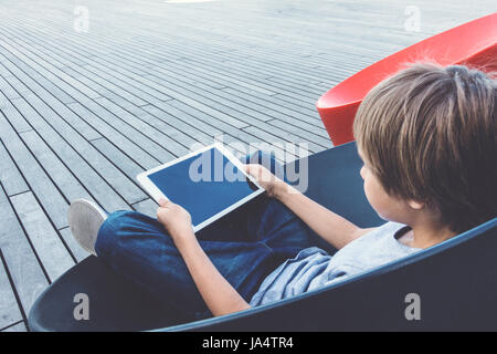 Enfant avec ordinateur tablette assis à l'extérieur. Banque D'Images