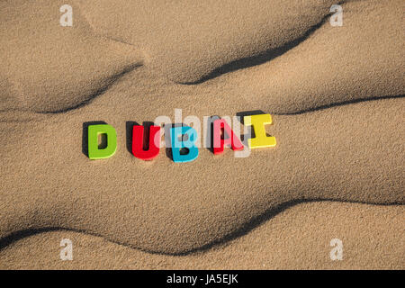 Lettres « DUBAÏ » aux couleurs vives gravées dans le sable doux du désert, créant un contraste saisissant et saisissant avec le paysage sablonneux Banque D'Images