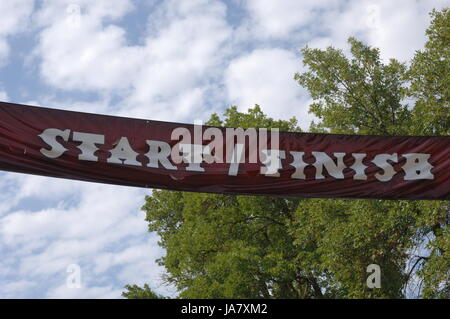 Ligne de départ et d'arrivée pour l'enseigne une course cycliste. Ciel bleu avec nuages gonflés et d'arbres. Commencer et finir en lettres blanches sur une bannière rouge passe Banque D'Images