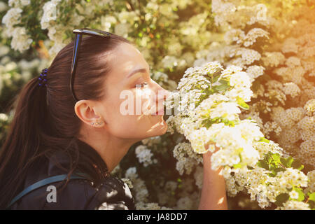 Lifestyle thème. Heureux brunet fleurs blanc odeur close-up. Portrait de jeune femme aux yeux clos. Banque D'Images