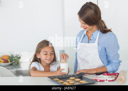 Petite fille tremper un biscuit dans un verre de lait dans la cuisine Banque D'Images