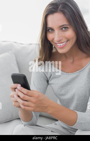 Portrait d'une femme textos alors qu'elle est assise sur un canapé Banque D'Images