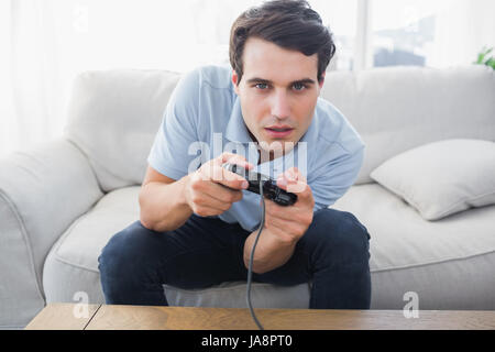 Homme concentré s'amusant avec les jeux vidéos alors qu'il est assis sur un canapé Banque D'Images