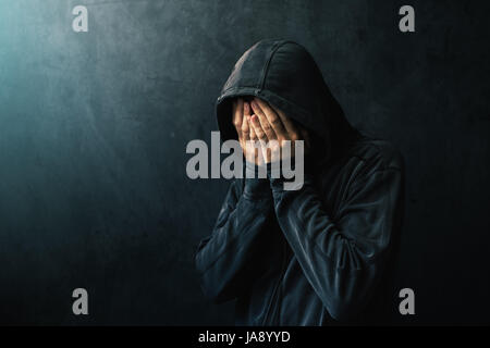 Homme désespéré en veste en pleure, les mains sont couvrant le visage et des larmes dans les yeux, la lumière de l'espoir de lumière venant de son côté droit Banque D'Images