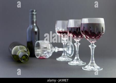 Concept de la consommation d'alcool, l'alcoolisme et l'abus par une ligne de beaux verres de cristal rempli de vin rouge, un plein et une bouteille vide. Étapes Banque D'Images