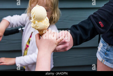 Un adulte donnant un cornet de crème glacée à un enfant. Banque D'Images