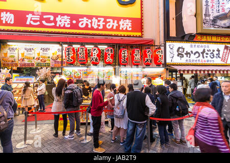 Dotonbori, Osaka. Les gens faire la queue pour acheter des aliments traditionnels japonais, Okonomiyaki et Takoyaki de comptoir à emporter au cours de la soirée. Banque D'Images