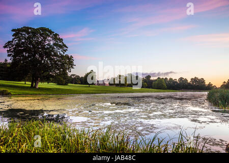 Un lever du soleil d'été sur le lac au parc Lydiard à Swindon, Wiltshire vers Lydiard House et St.Mary's Church dans la distance. Banque D'Images