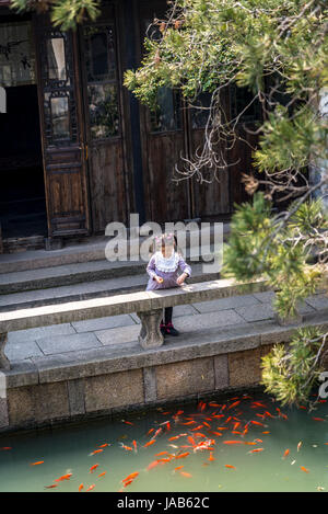 Petite fille nourrir les poissons dans un étang, heureux de l'eau Agriculture Hall, ancienne ville de Tongli, Suzhou, Province de Jiangsu, Chine Banque D'Images