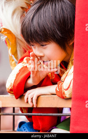 L'enfant japonais, garçon, 8-9 ans, penché sur la rampe en bois qu'il parle à quelqu'un (main invisible) rondelles autour de la bouche comme s'appelant somone. Banque D'Images