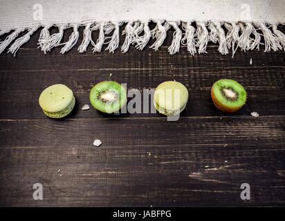 Macarons et kiwi vert comme une frontière sur une nappe blanche avec fond en bois Banque D'Images