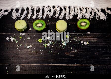 Macarons et kiwi vert comme une frontière sur une nappe blanche avec fond en bois Banque D'Images