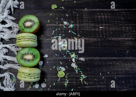 Macarons et kiwi vert comme une frontière sur une nappe blanche avec fond en bois Banque D'Images