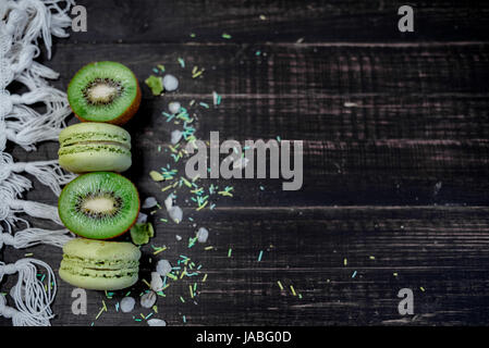 Macarons et kiwi vert comme une frontière sur une nappe blanche avec fond en bois Banque D'Images