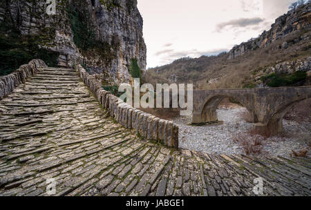 - Noutsou kokkori vieux pont en pierre voûtée sur le canyon de vikos, zagorochoria, Grèce. hiver coucher du soleil avec de la glace et des glaciers sur la rivière. Banque D'Images