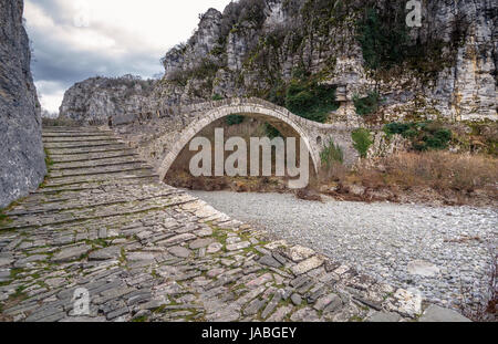 - Noutsou kokkori vieux pont en pierre voûtée sur le canyon de vikos, zagorochoria, Grèce. hiver coucher du soleil avec de la glace et des glaciers sur la rivière. Banque D'Images