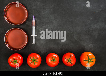 Aliments génétiquement modifiés de tomate sur le tableau situé à l'arrière-plan avec de belles tomates fraîches et de fruits rouge clair liquide dans la seringue. Banque D'Images