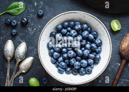 Still Life de bleuets frais dans un bol, des couverts bébé vintage, kiwi et épinards sur table en pierre. Vue de dessus, gros plan Banque D'Images