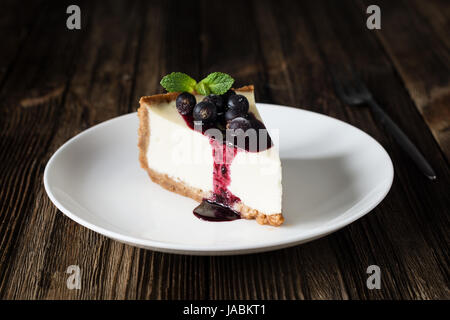 Morceau de gâteau au fromage avec sauce aux bleuets et de cassis sur plaque blanche sur table en bois. Vue rapprochée Banque D'Images