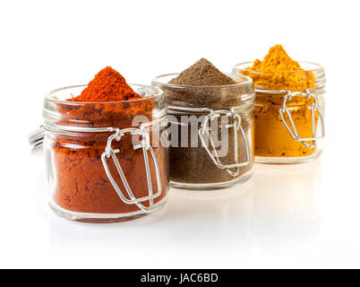 Trois pots de verre remplis d'épices dont la masse colorée, de chili et de curry, de cannelle sur un fond blanc Banque D'Images